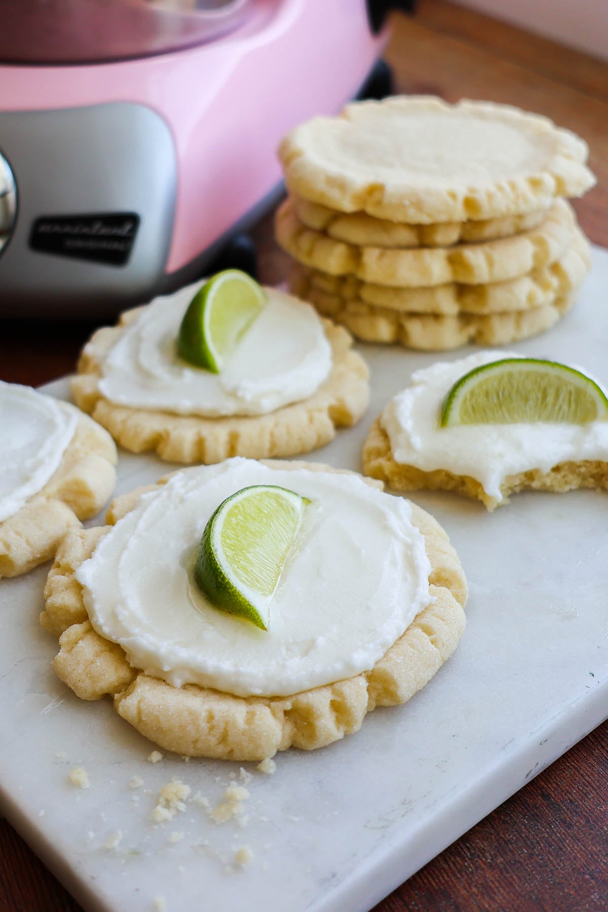 Several frosted coconut lime sugar cookies, each with. a wedge of lime on top.