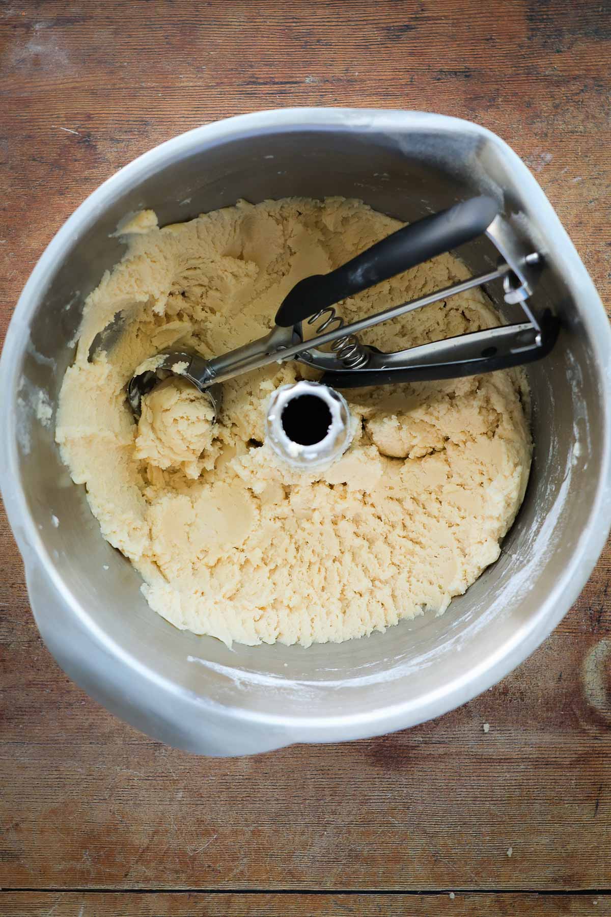 A mixer bowl full of sugar cookie dough, with. a cookie scoop resting on it.