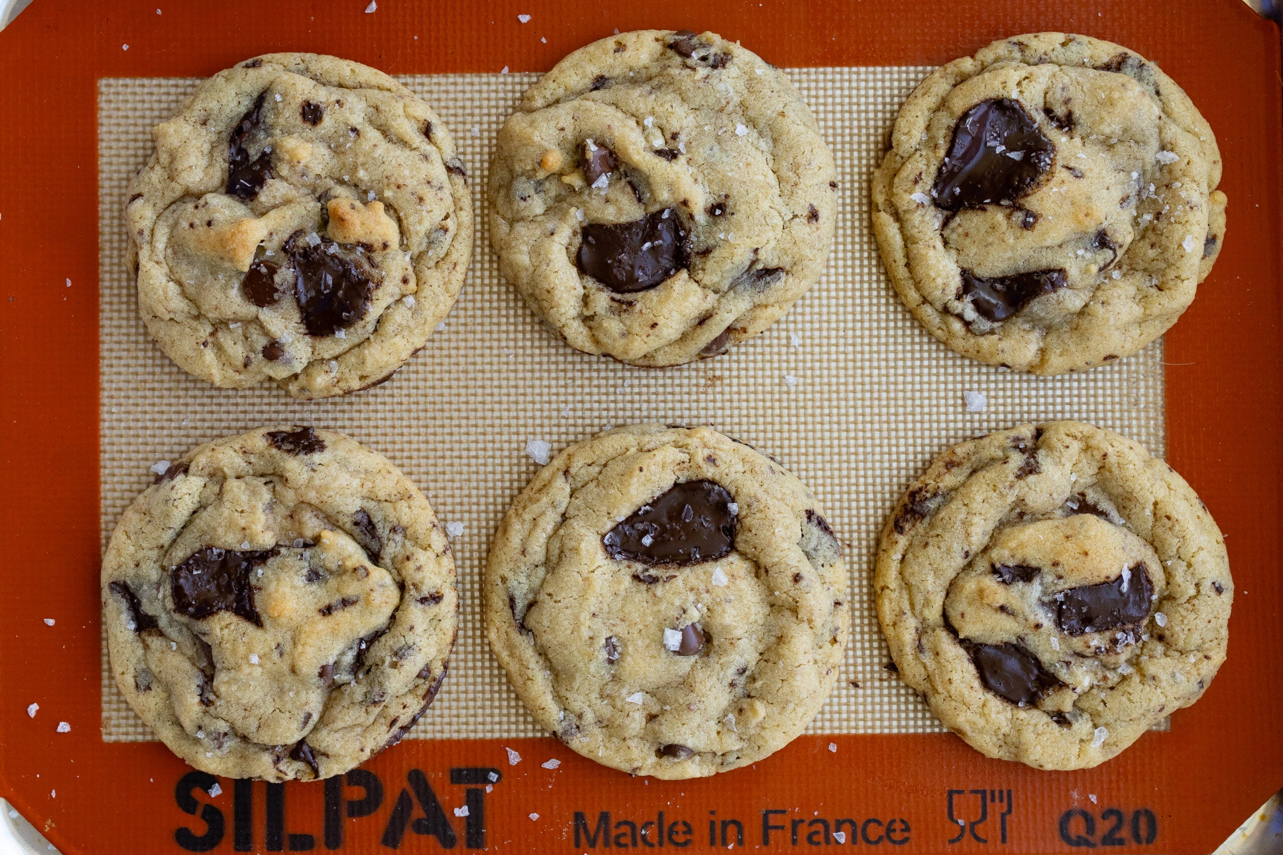 Baked Brown Butter Sourdough Chocolate Chip Cookies with sea salt flakes on top, on a baking sheet lined with a silicone baking mat.