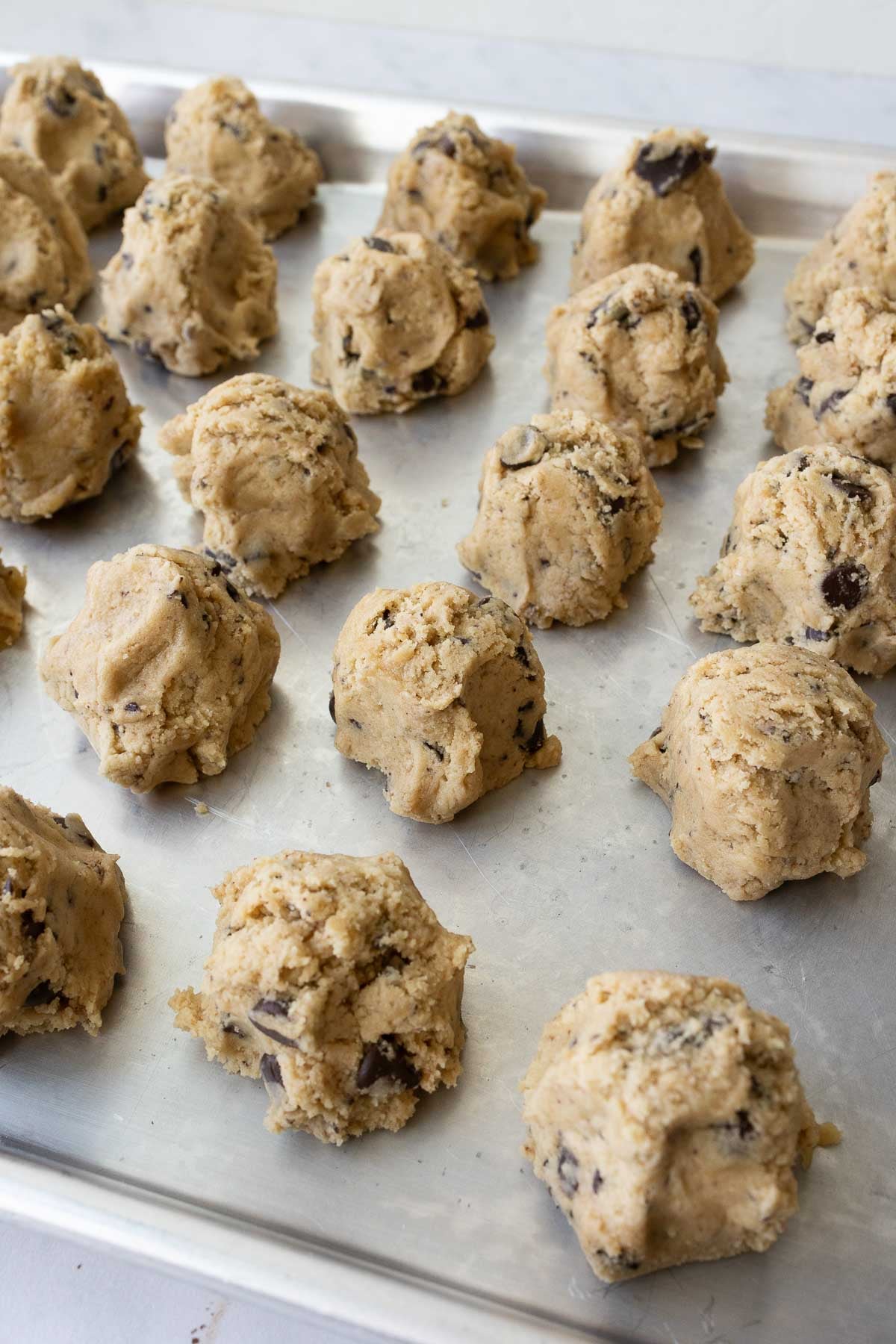 Several balls of chocolate chip cookie dough on a bking sheet.