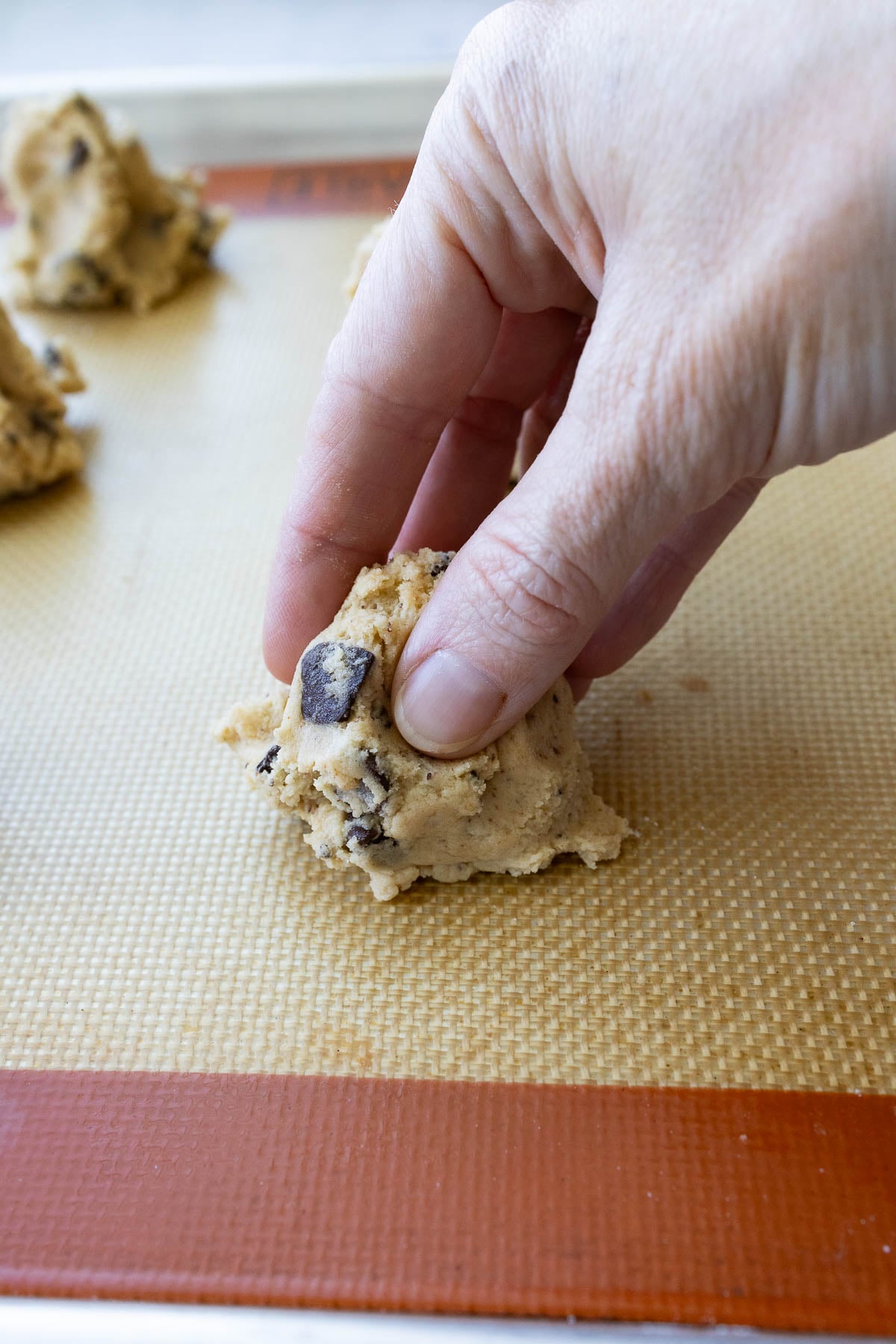 A hand pinching a ball of brown butter sourdough chocolate chip cookie dough.