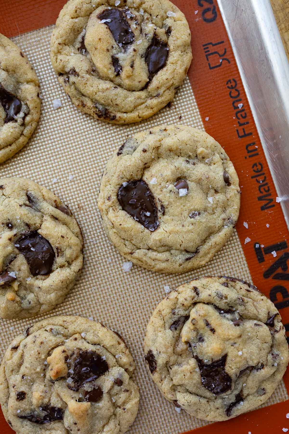 Sourdough brown butter chocolate chip cookies on a baking sheet lined with a silicone baking mat.