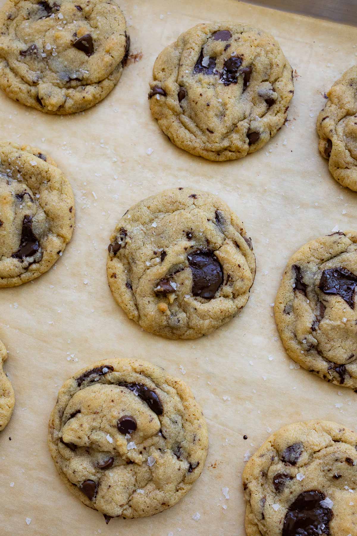 Baked brown butter sourdough chocolate chip cookies with sea salt flakes on top, resting on a baking sheet lined with parchment paper.