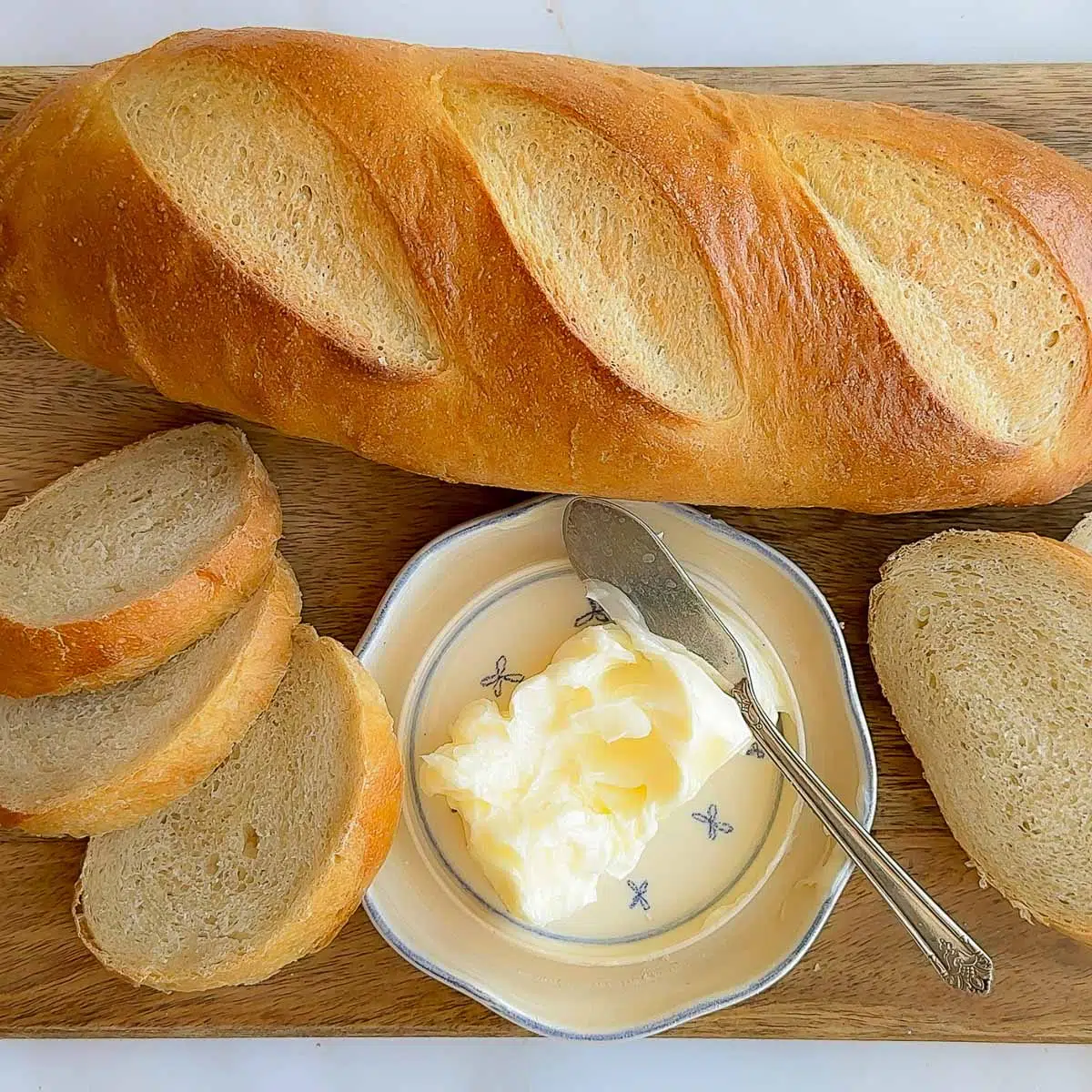 A loaf of French bread on a wood cutting board, with sliced French bread and butter.