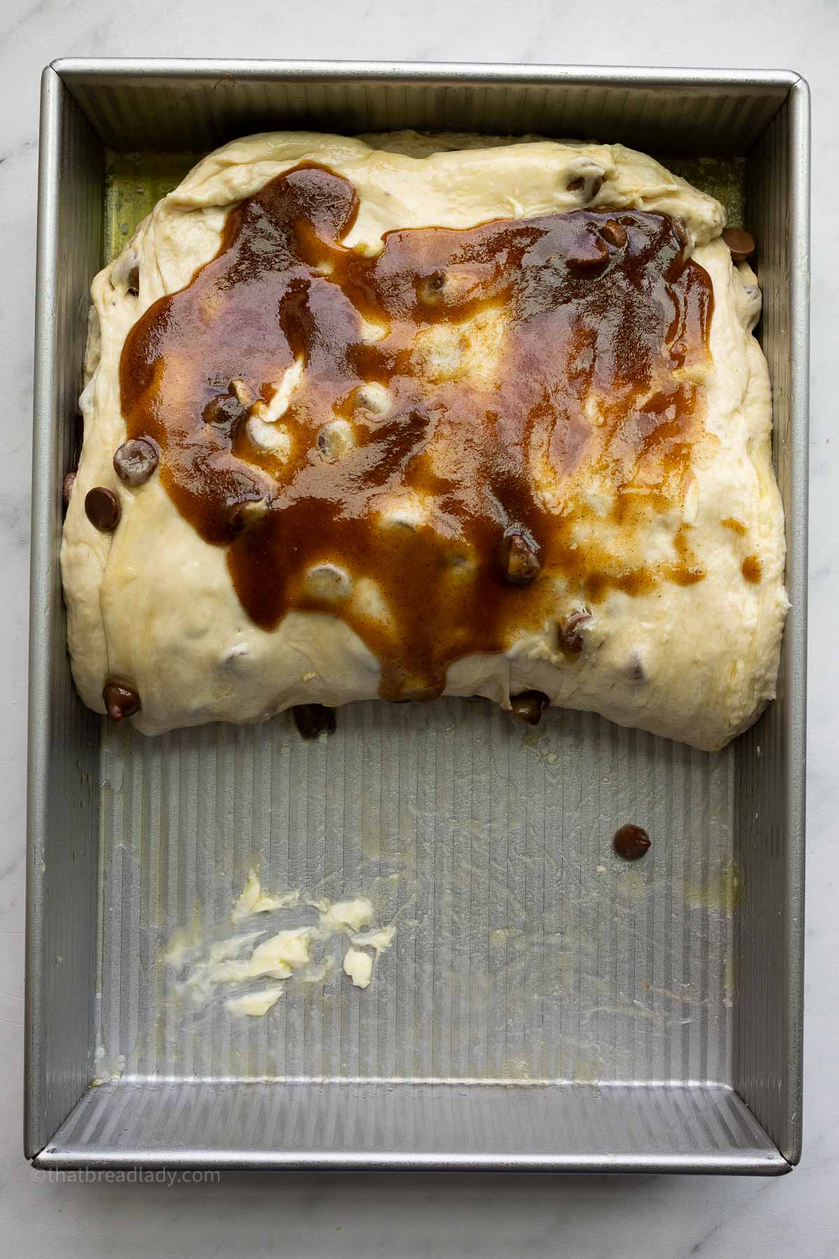 Chocolate chip banana bread focaccia dough in a 9x13-inch metal cake pan, with the dough folded in half and cinnamon sugar filling spread over the dough.