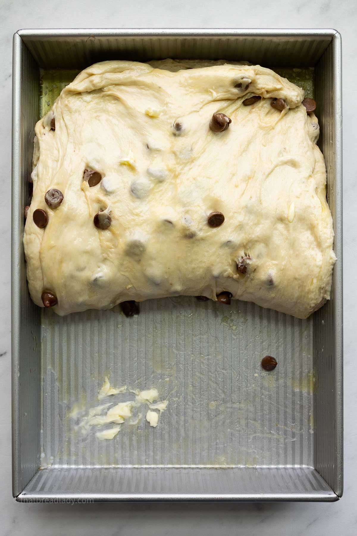 Chocolate chip banana bread focaccia dough in a 9x13-inch metal cake pan, with the dough folded in half.