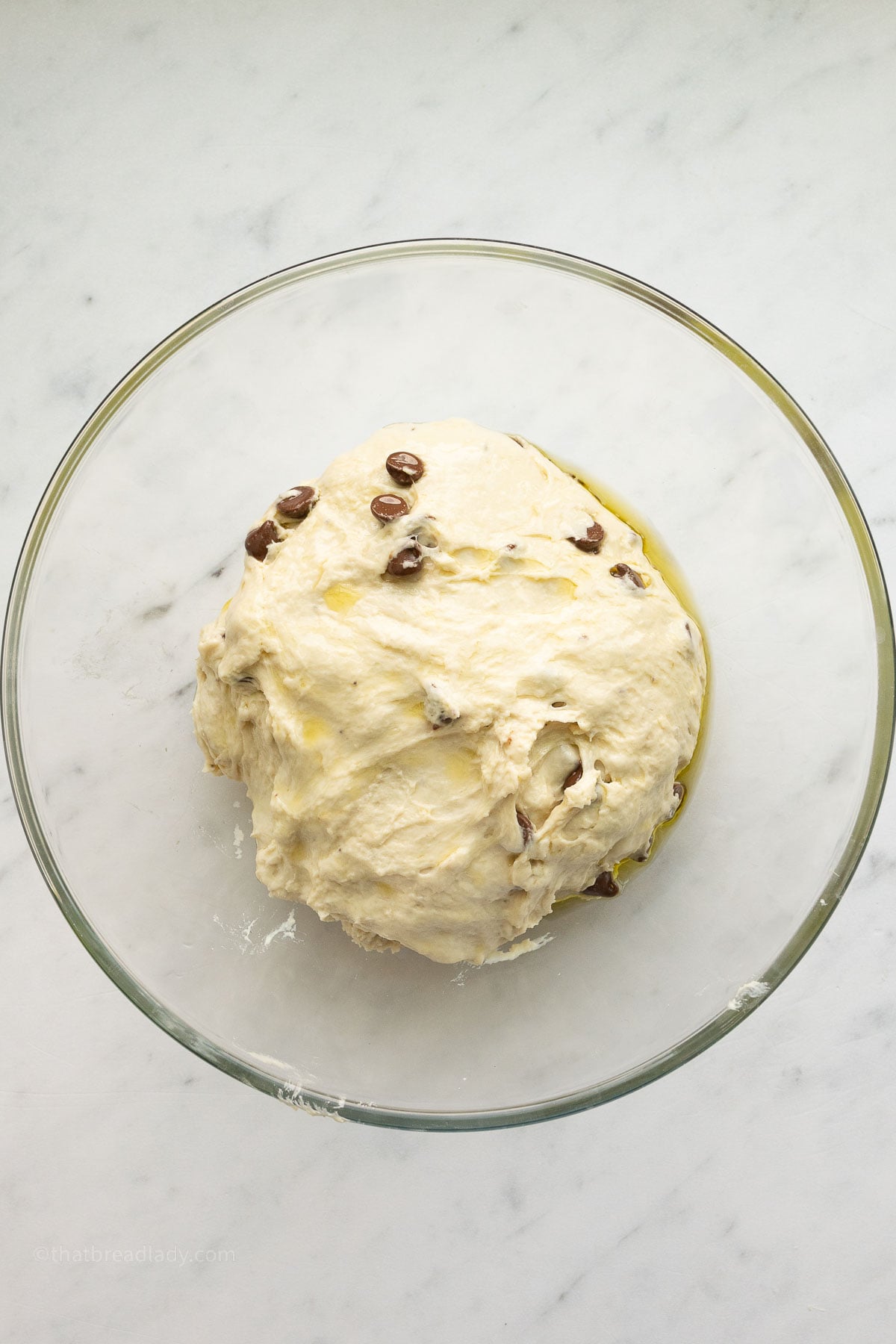Chocolate chip banana bread focaccia dough in a glass bowl, coated with olive oil.
