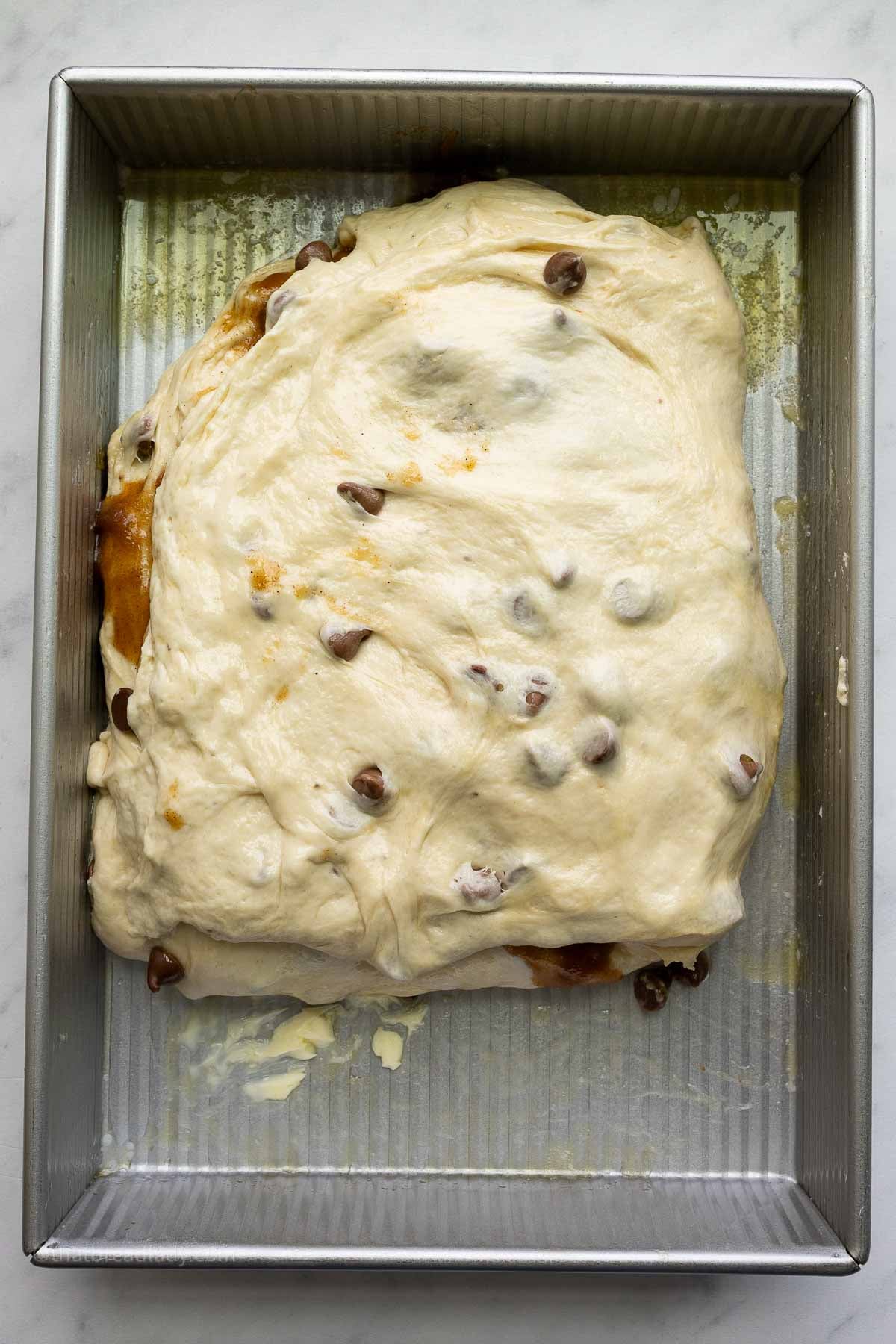 Chocolate chip banana bread focaccia dough in a 9x13-inch metal cake pan, with the dough folded in half, not quite filling the pan.