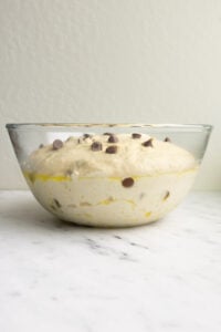 A glass bowl with risen chocolate chip banana bread focaccia.