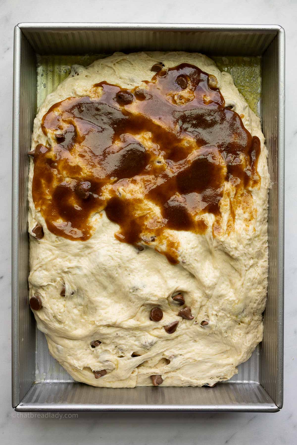 Chocolate chip banana bread focaccia dough in a 9x13-inch metal cake pan, with cinnamon filling spread over the top half of the dough.