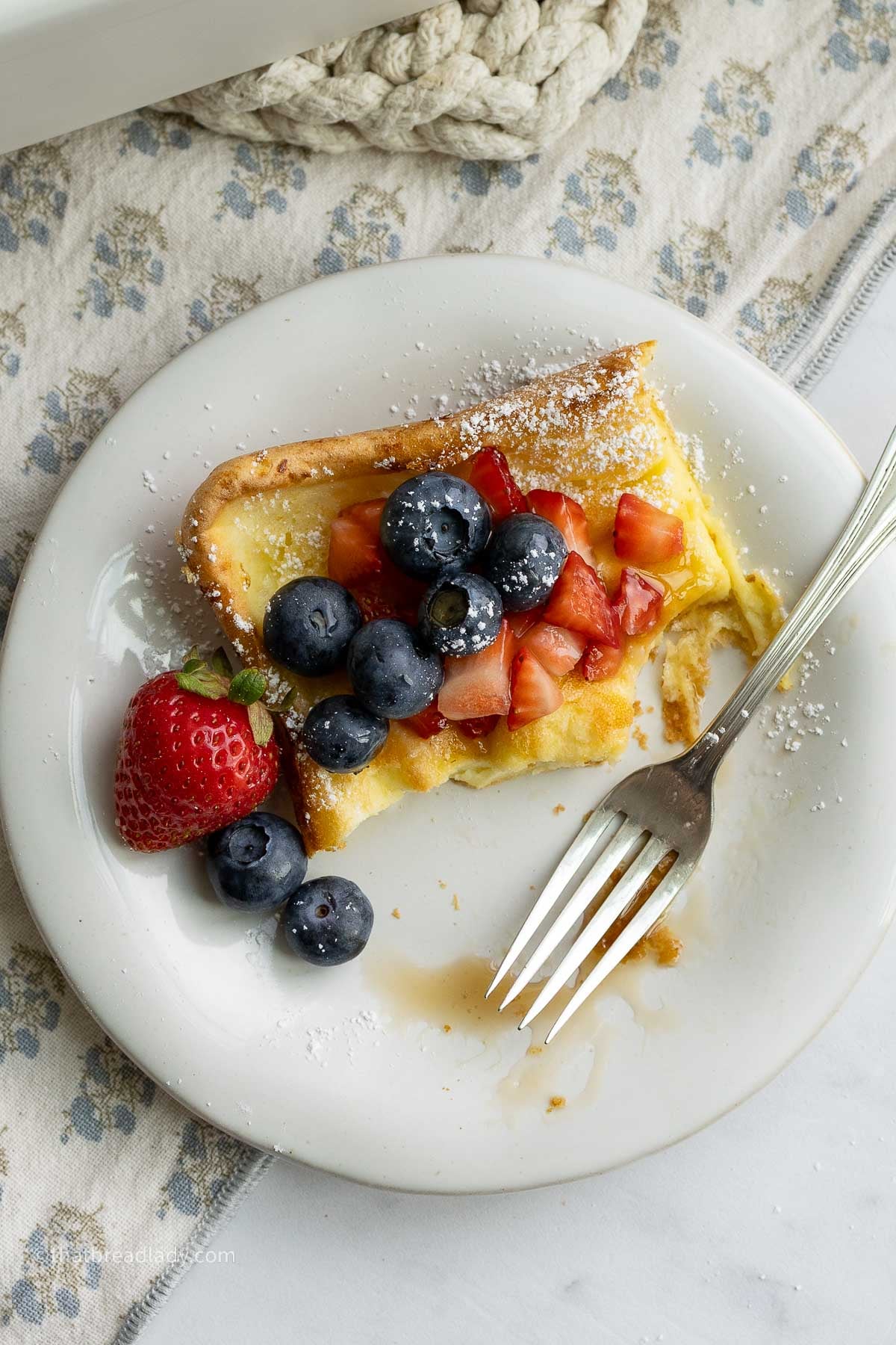 A dessert plate with a slice of sourdough Dutch baby pancakes, and strawberries and blueberries, and a fork.