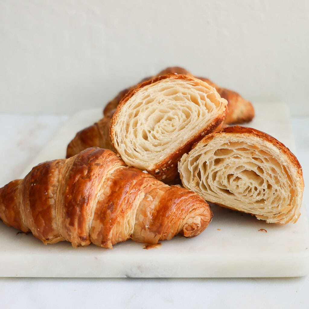 Croissants on a marble tray, with one whole croissant, and a croissant sliced in half.
