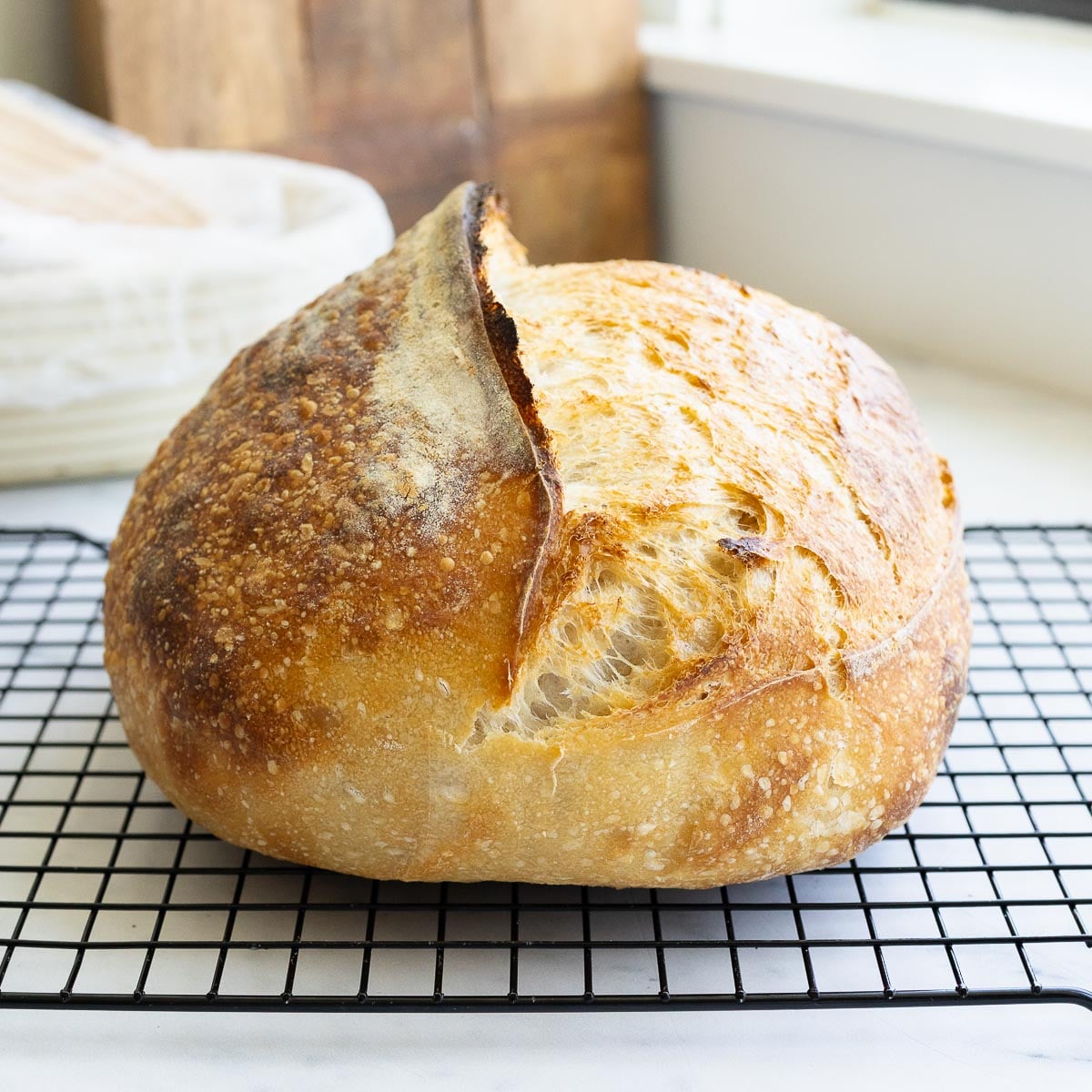 A loaf of baked sourdough bread on a wire cooling rack.