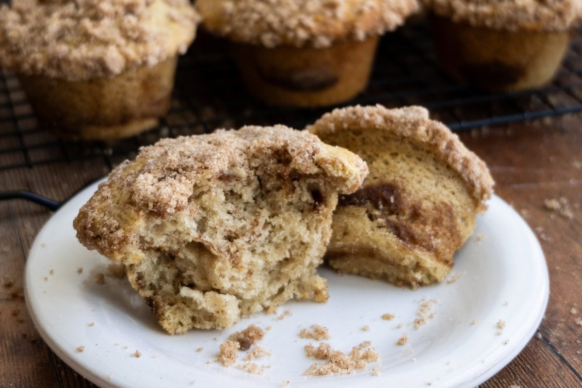 Sourdough coffee cake muffins on a wire cooling rack, a muffin split in half on a dessert plate.