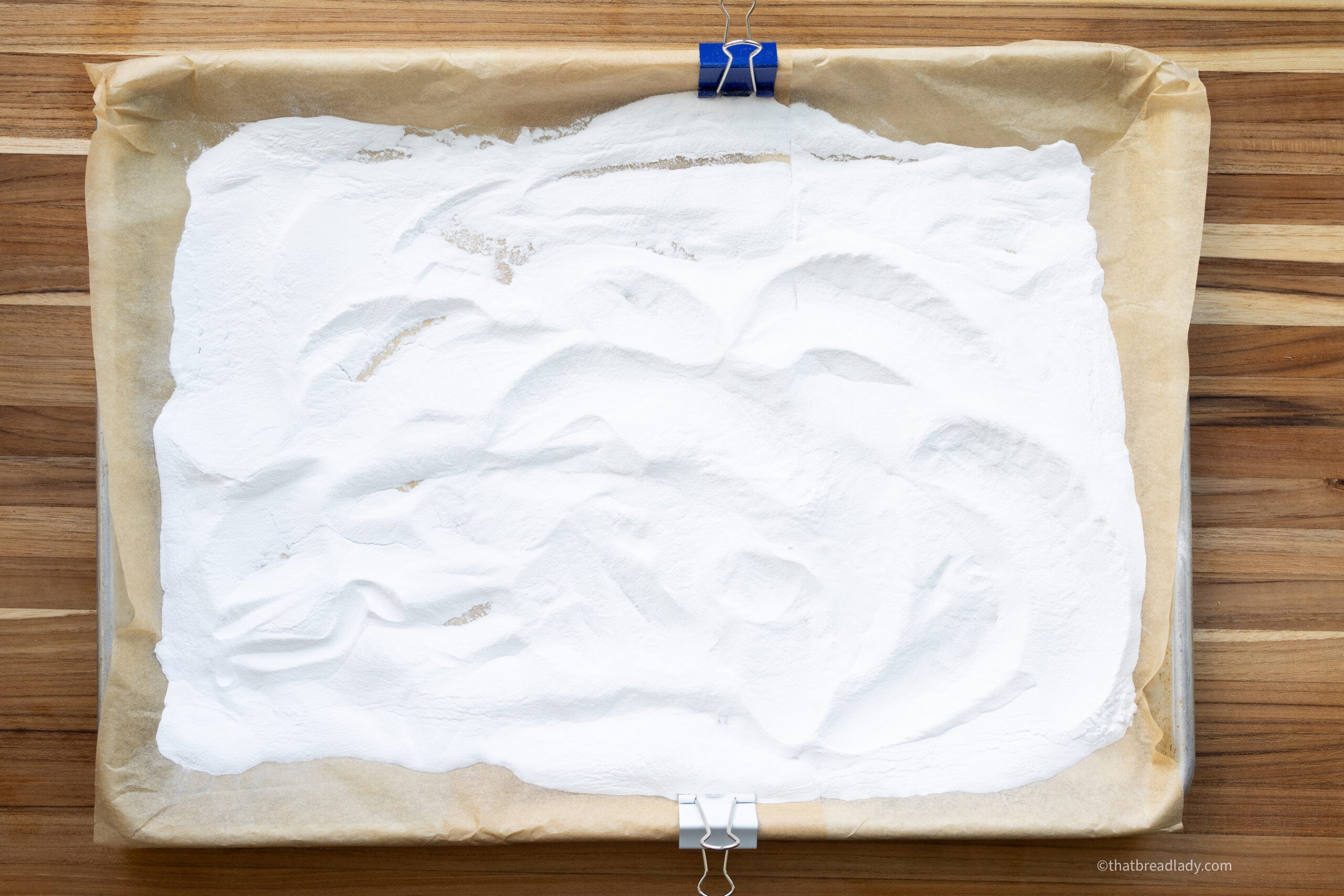 A baking sheet lined with parchment, kept in place with clips, and baking soda on the baking sheet.