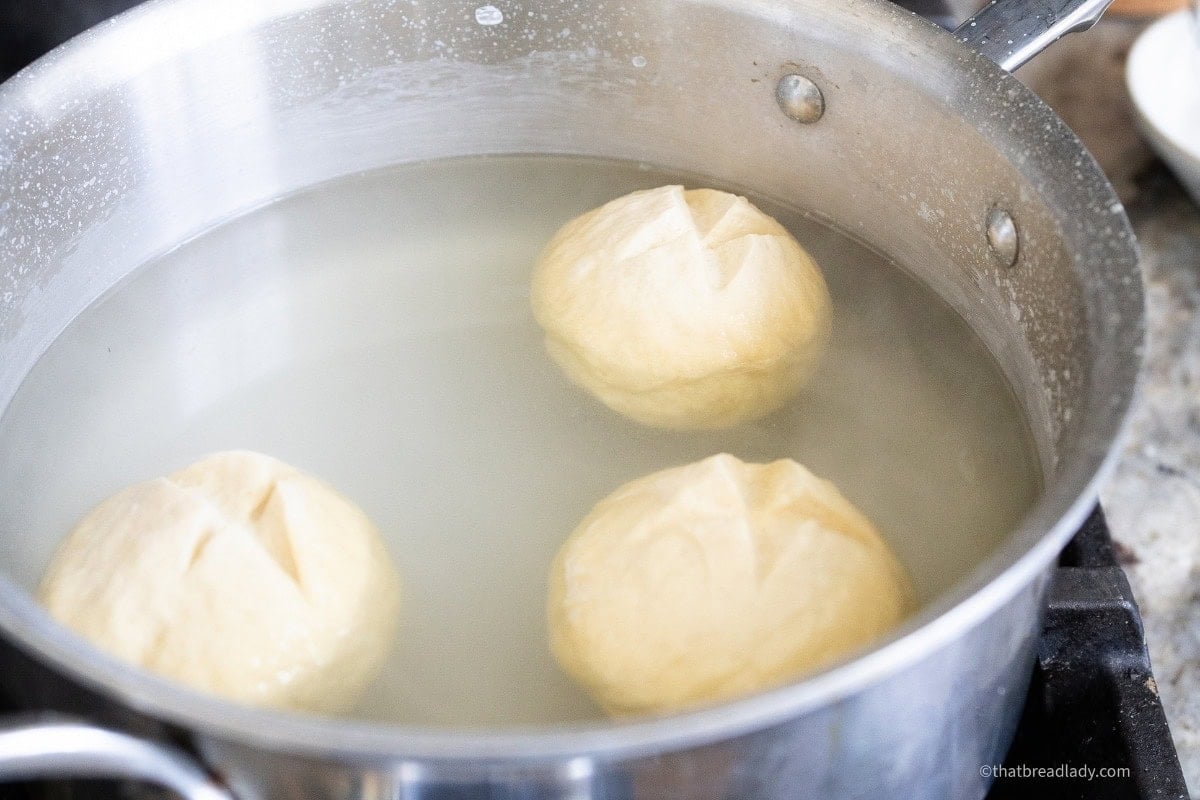 Three soft pretzel rolls, floating in water in a saucepan.
