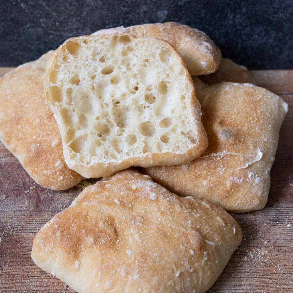 Ciabatta rolls, with one sliced open, resting on a wood board.