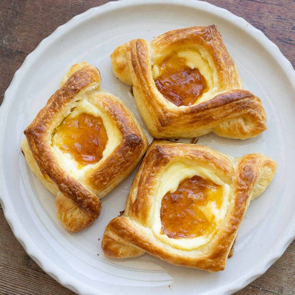 Three apricot cream cheese Danish pastries on a plate.