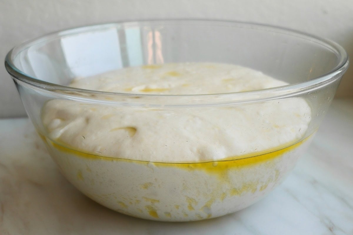 A glass bowl with risen focaccia dough in it.