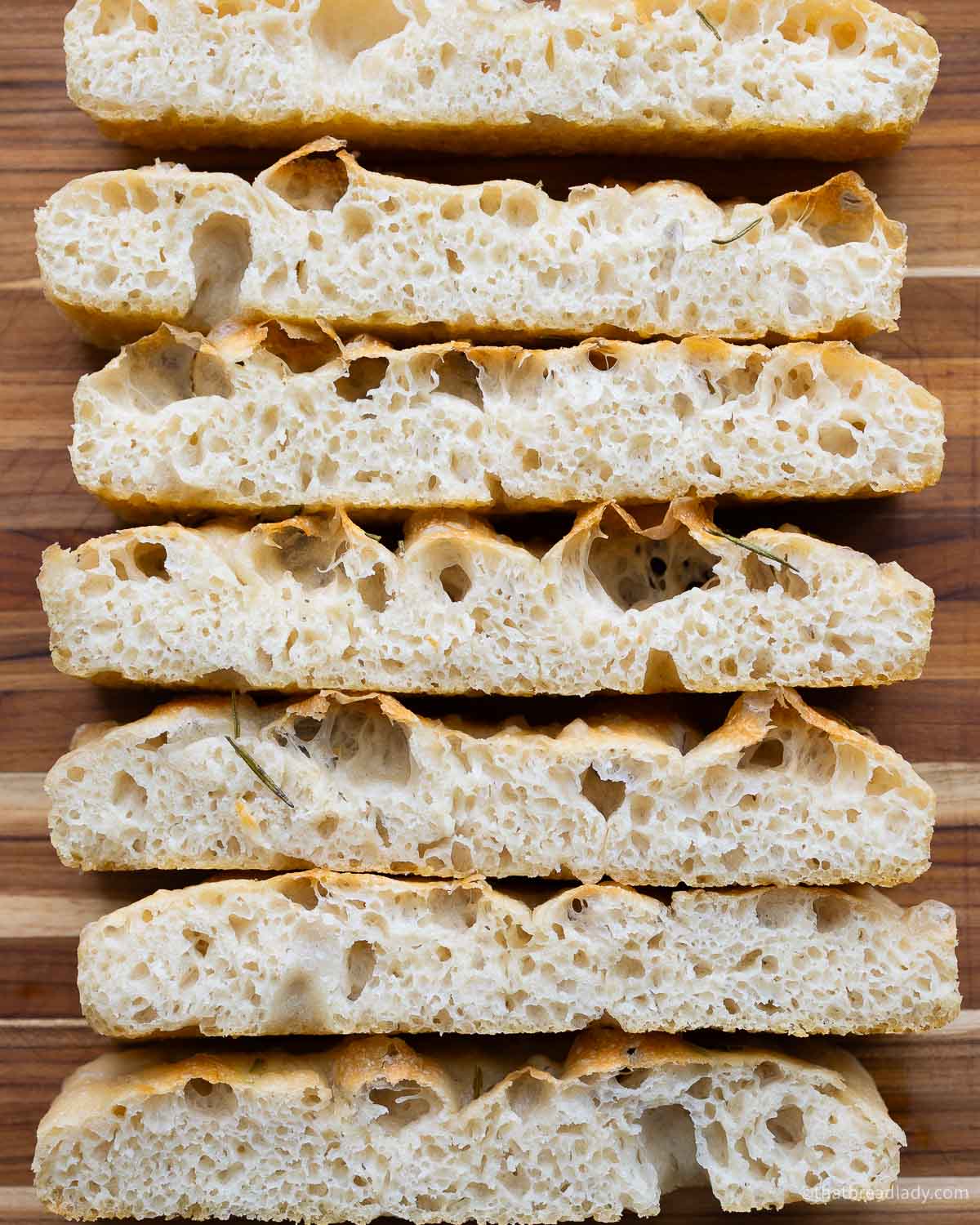 Slices of focaccia, laying on their sides, resting on a wood cutting board.