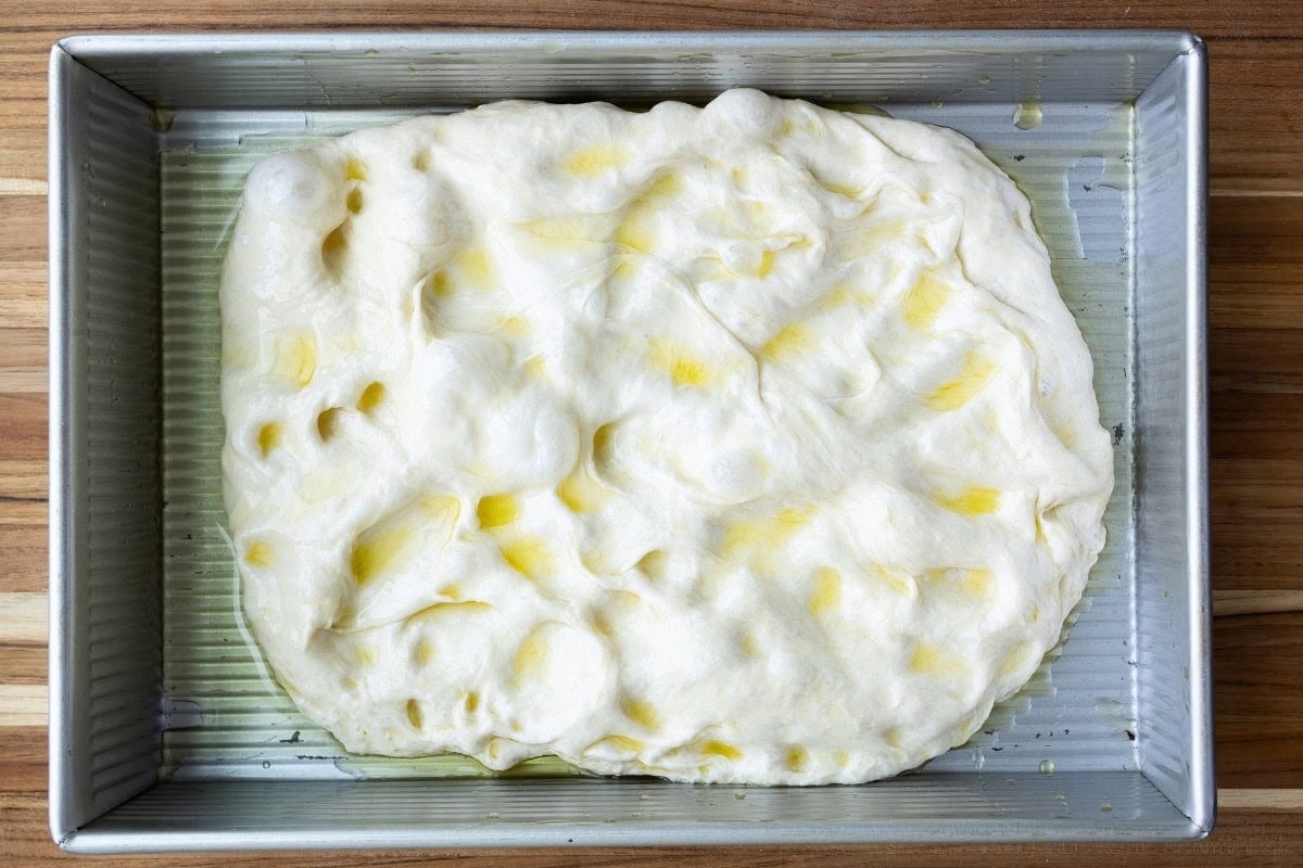 A pan with focaccia dough and olive oil on top, not quite filling the pan.