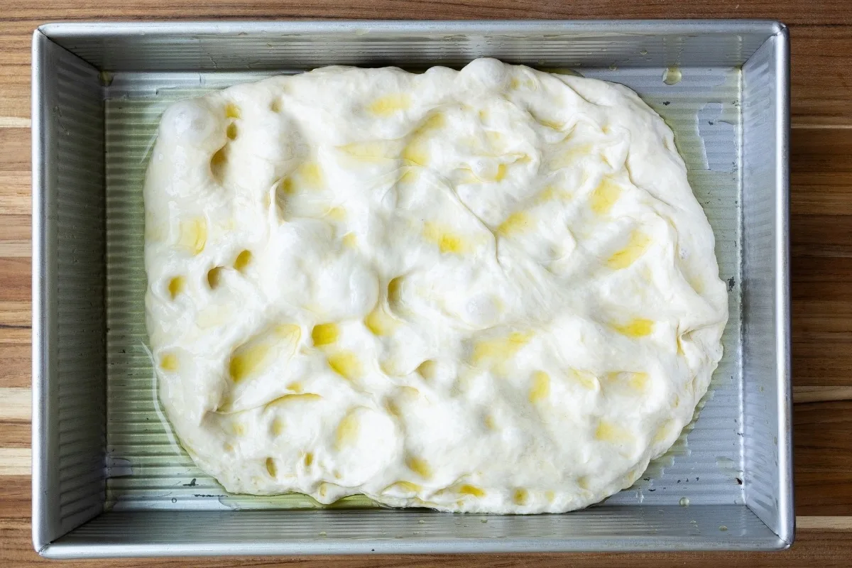 A pan with focaccia dough and olive oil on top, not quite filling the pan.