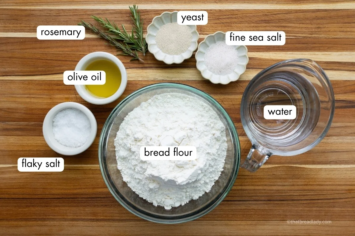 The ingredients for focaccia bread, in individual bowls, on a wood cutting board.