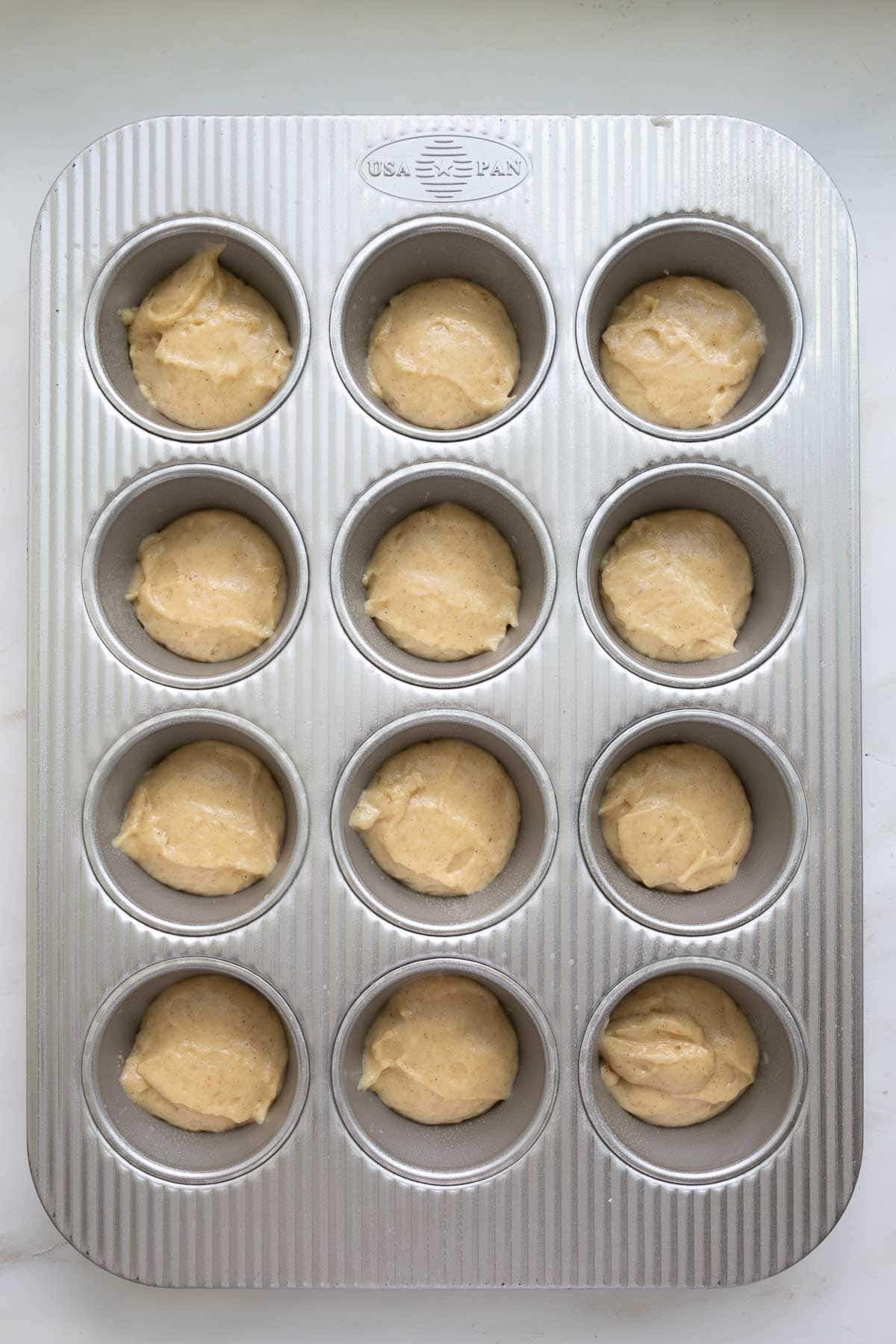A metal muffin tin with sourdough coffee cake muffin batter in each cup.